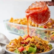 hand pouring catalina dressing over taco salad.