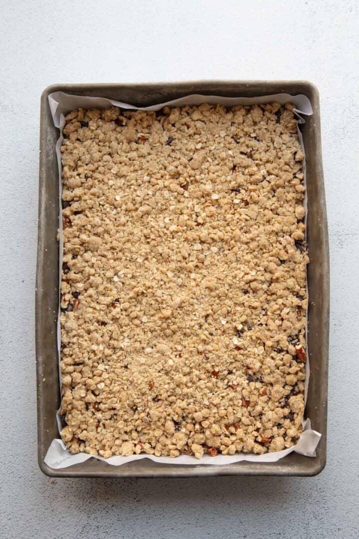 oatmeal crumble on top of caramel in a metal pan.