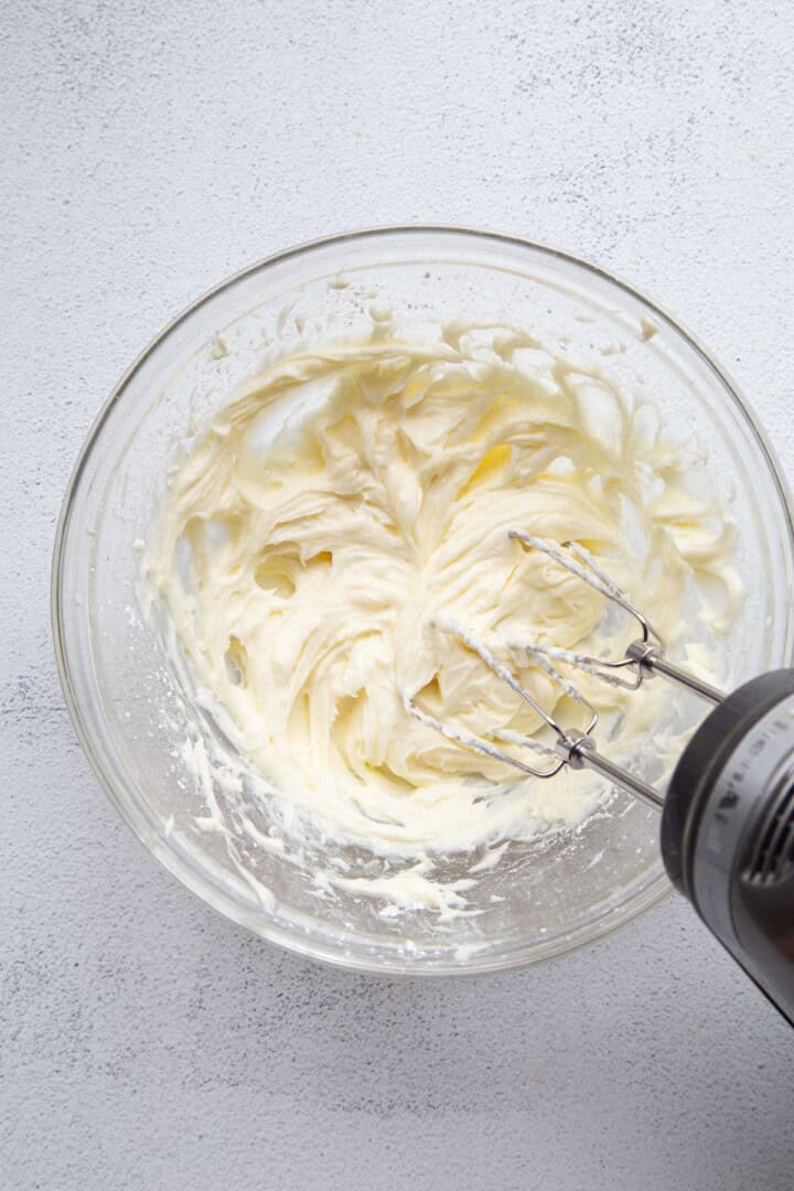cream cheese with a mixer in a glass bowl.