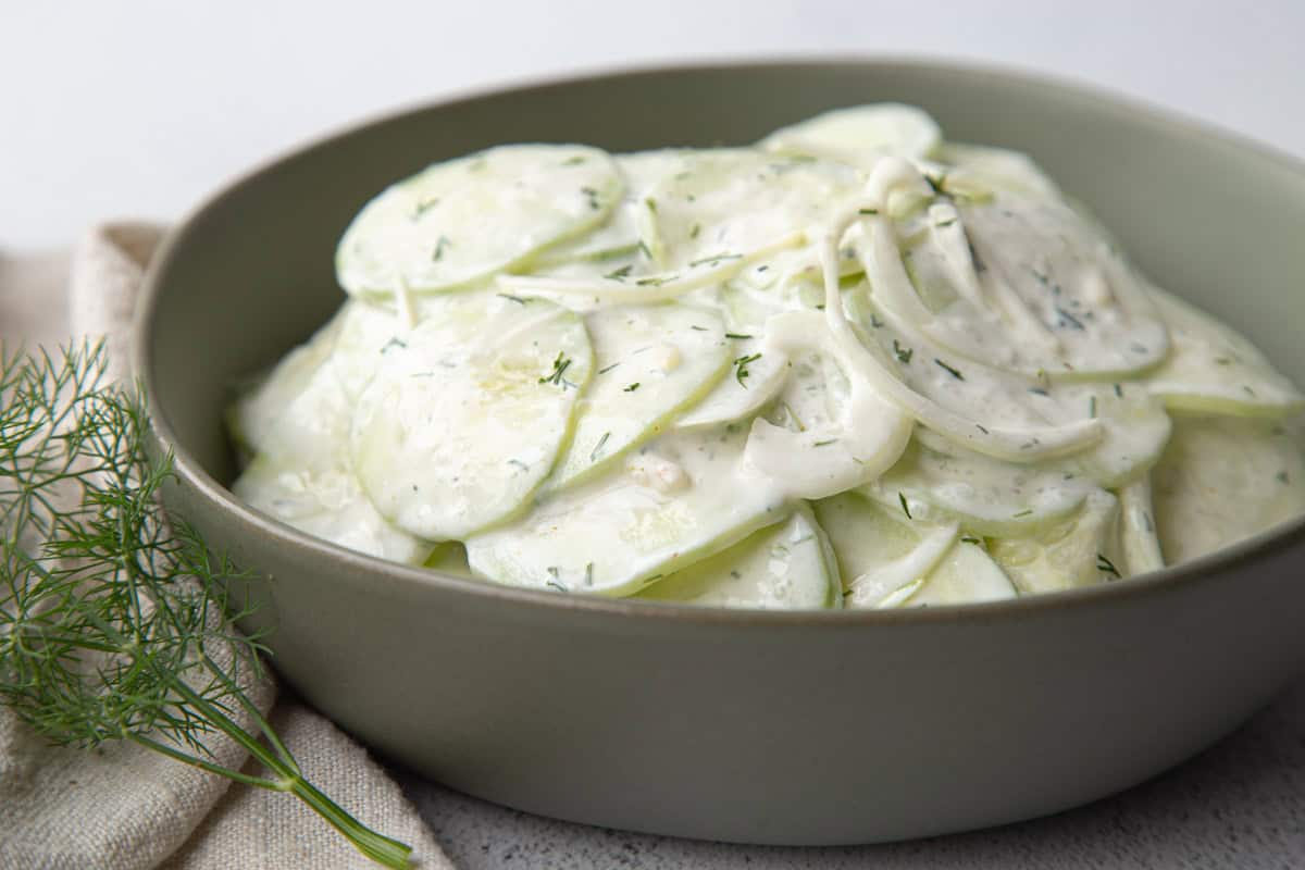 sour cream cucumbers and onions in a low green bowl.