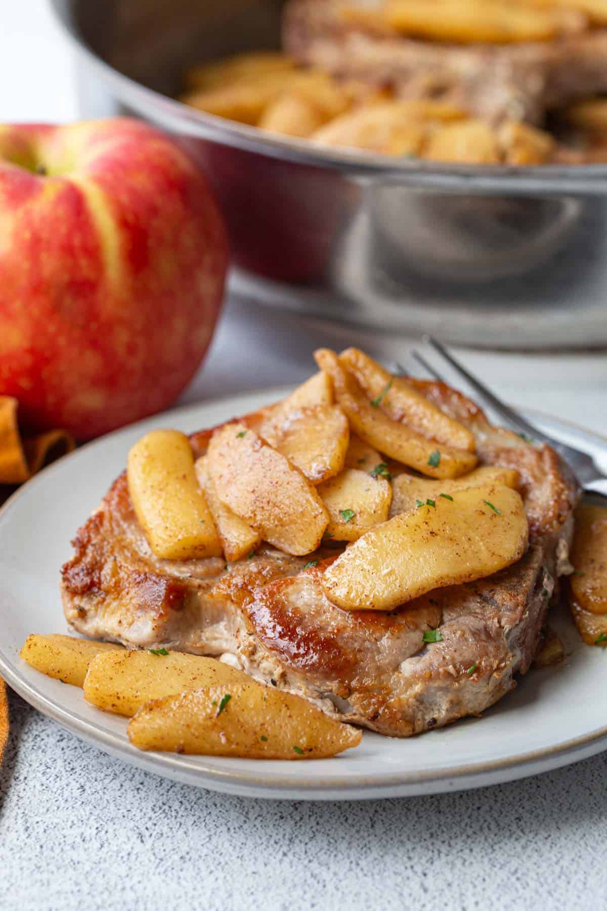 plate with a pork chop topped with apples.