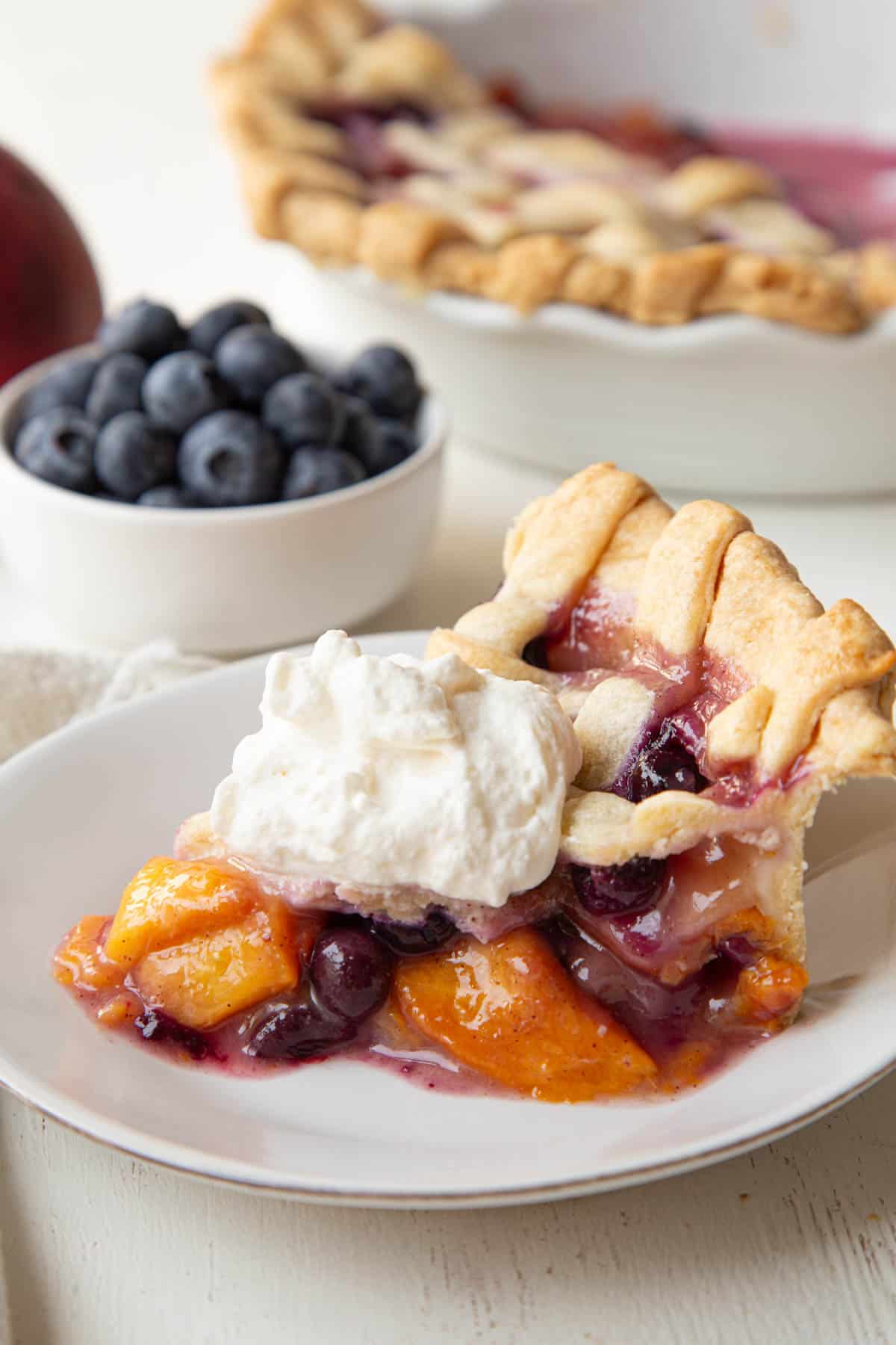slice of blueberry peach pie with whipped cream on top.
