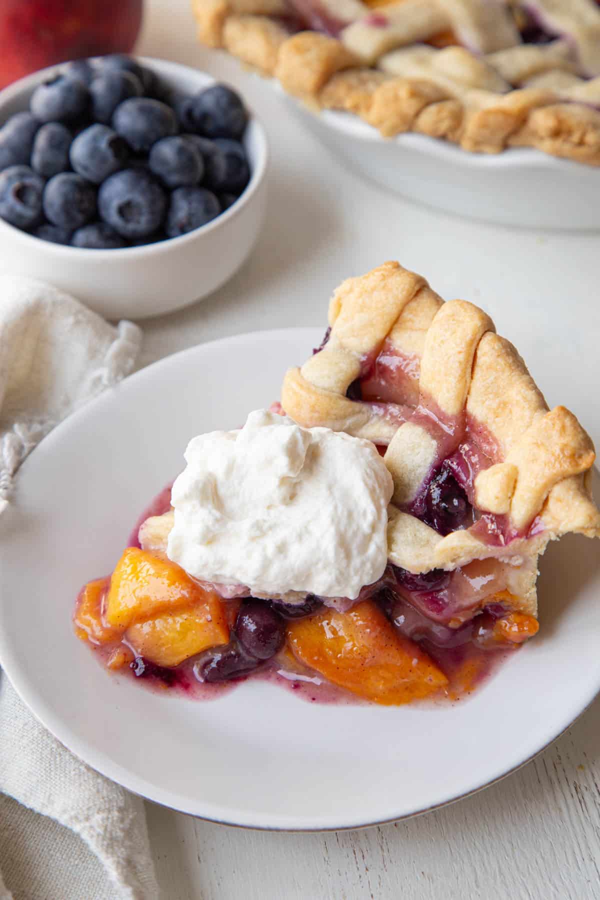 slice of peach blueberry pie with whipped cream.