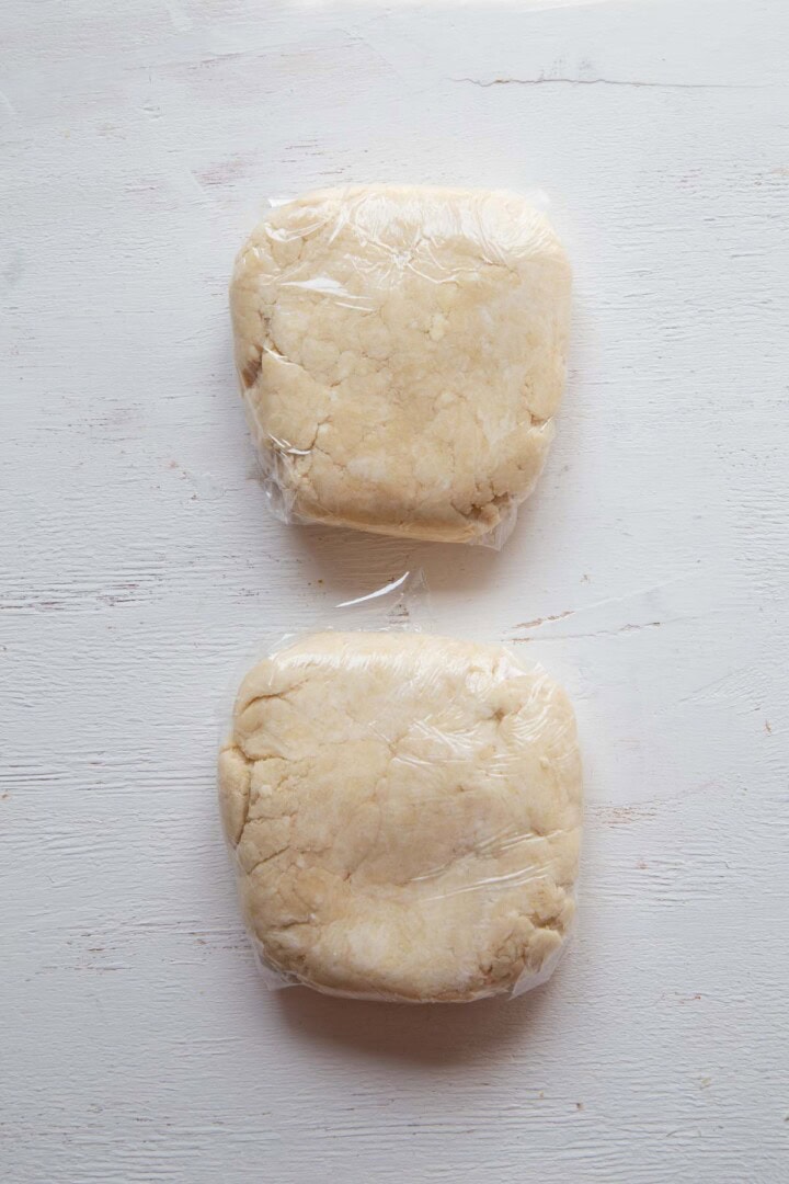 two disks of pie dough wrapped in plastic wrap.