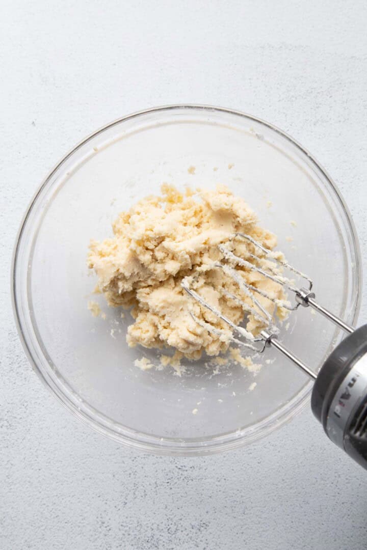 dough in a glass bowl with a hand mixer.