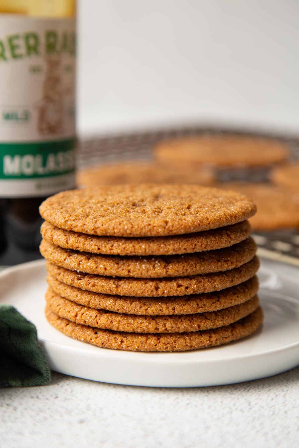 gingersnaps stacked on a white plate with a bottle of molasses.