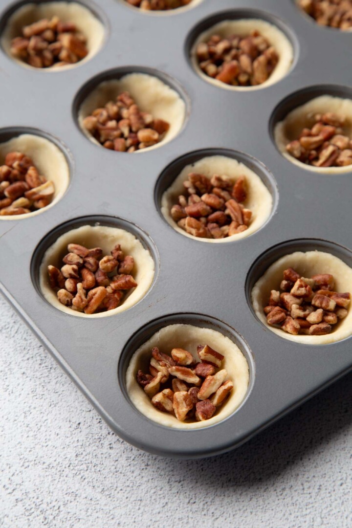 pecans in the bottom of mini muffin cups with dough.