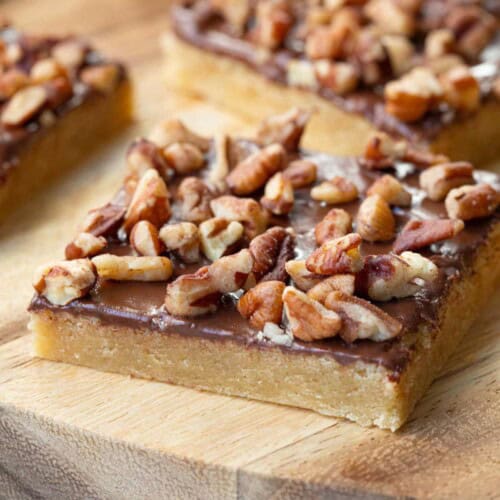 toffee squares topped with nuts on a wooden board.
