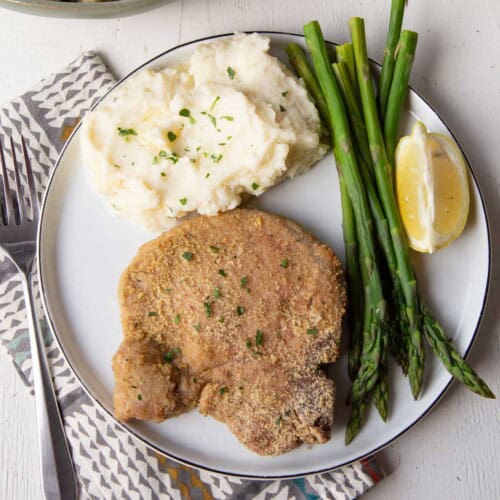 shake and bake pork chop on a plate with mashed potatoes and asparagus.