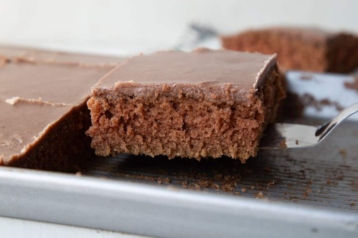 slice of chocolate texas sheet cake being lifting from a pan with a spatula.