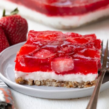 slice of a layered dessert with a pretzel crust, cream cheese filling, and strawberry gelatin on top.