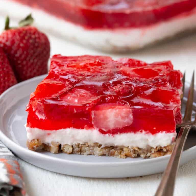 slice of a layered dessert with a pretzel crust, cream cheese filling, and strawberry gelatin on top.