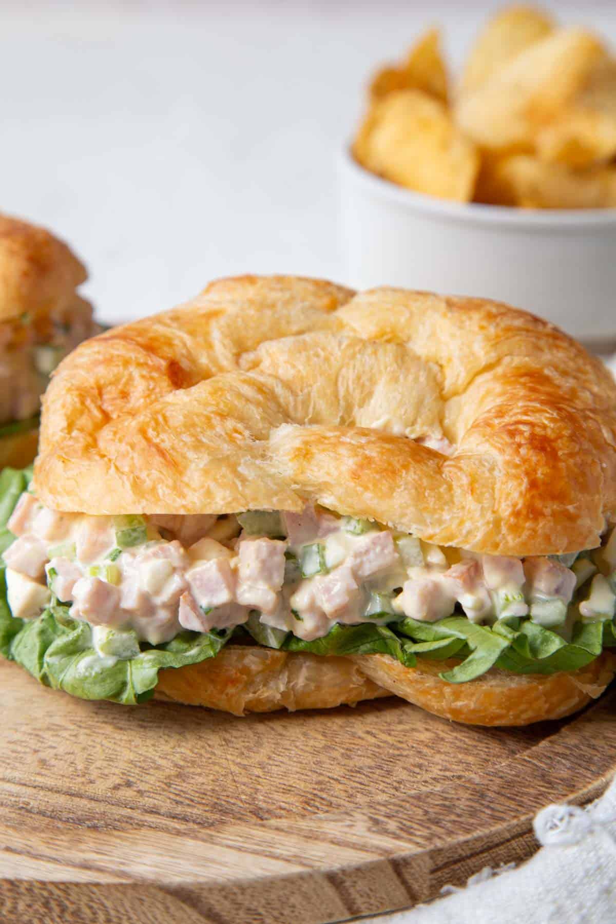 ham salad on a croissant with potato chips in the background.