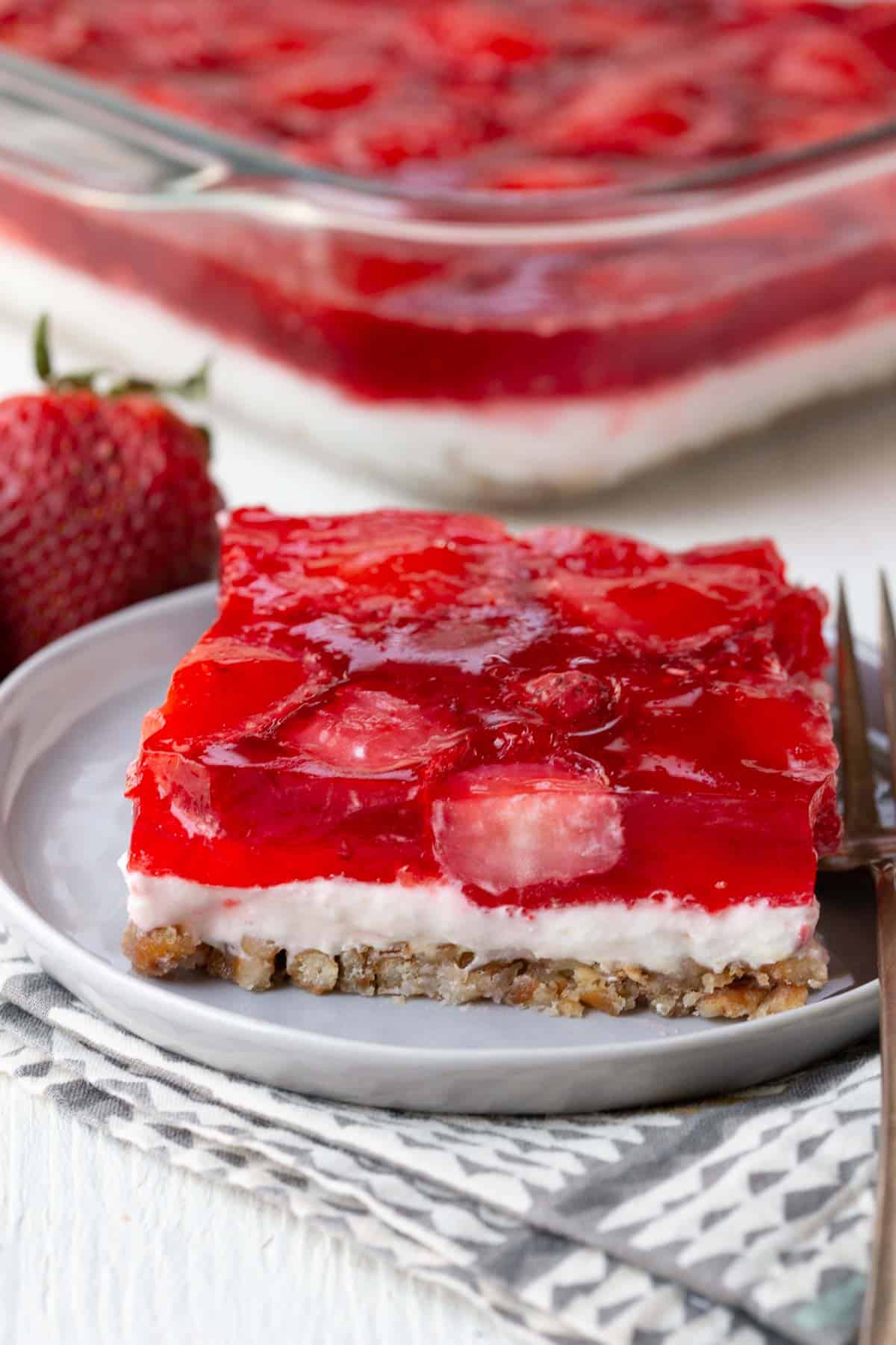slice of layered dessert with a pretzel crust, creamy center, and strawberry jello topping.