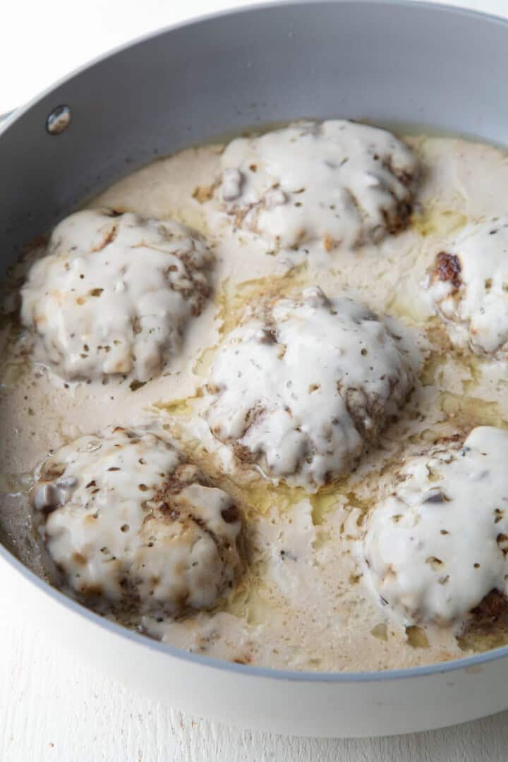 cooked beef patties covered with cream of mushroom soup in a skillet.