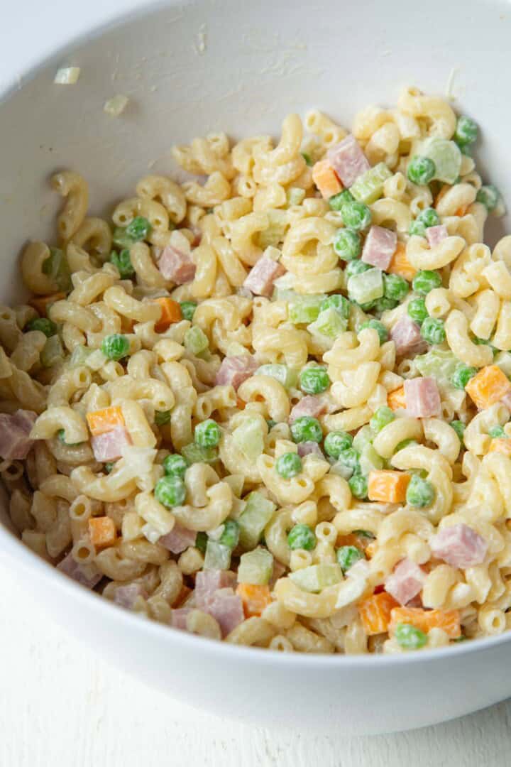 cooked macaroni tossed with peas, ham, and cheddar in a white bowl.