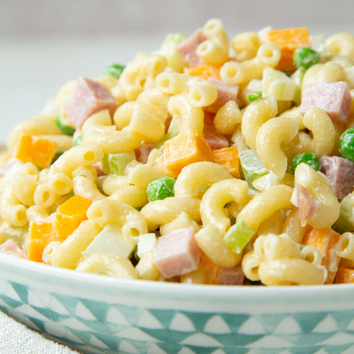 macaroni salad with ham, peas, and cheddar in a blue and white bowl.