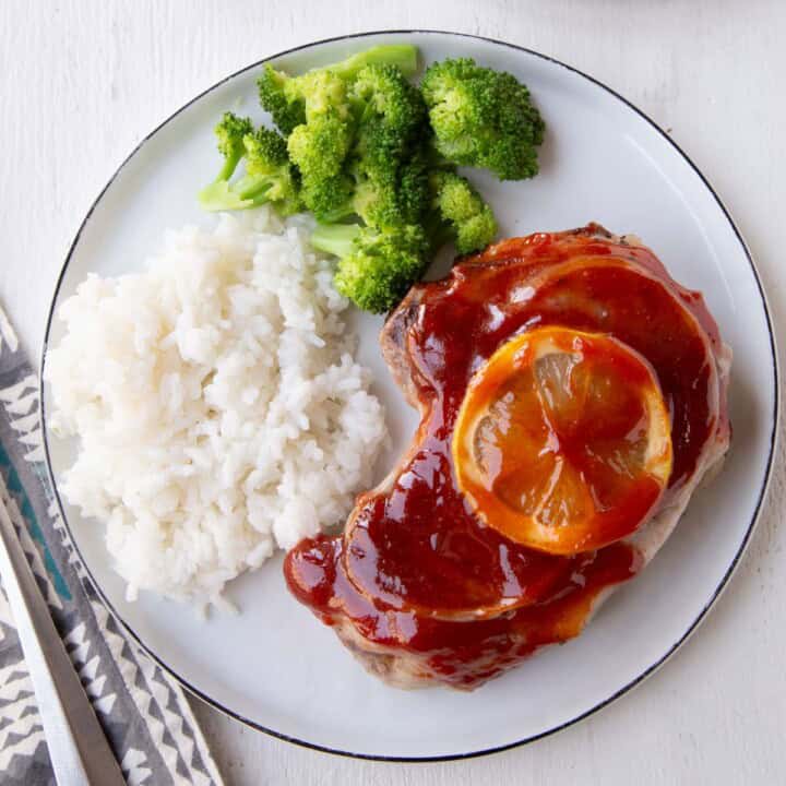 pork chop covered in red sweet and sour sauce with rice and broccoli.
