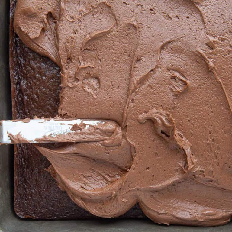 chocolate fudge frosting being spread onto a chocolate cake.
