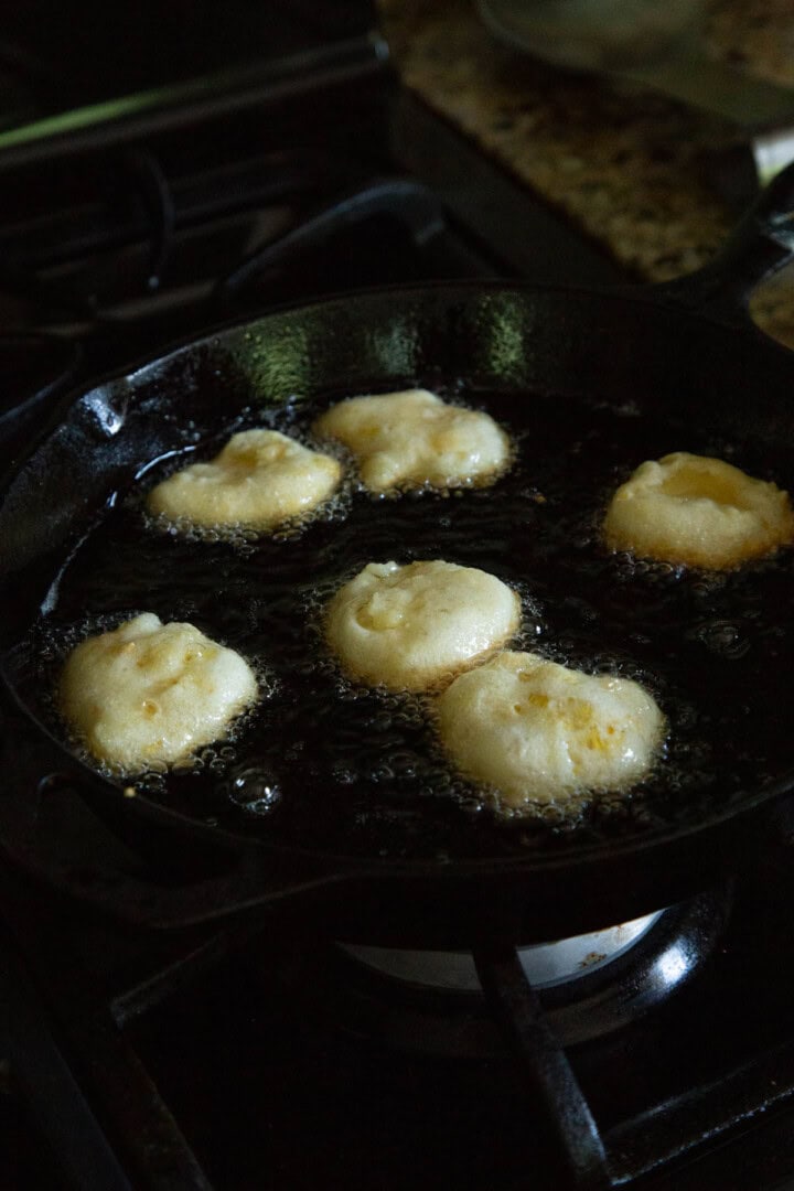 corn fritters partially cooked in oil in a skillet.