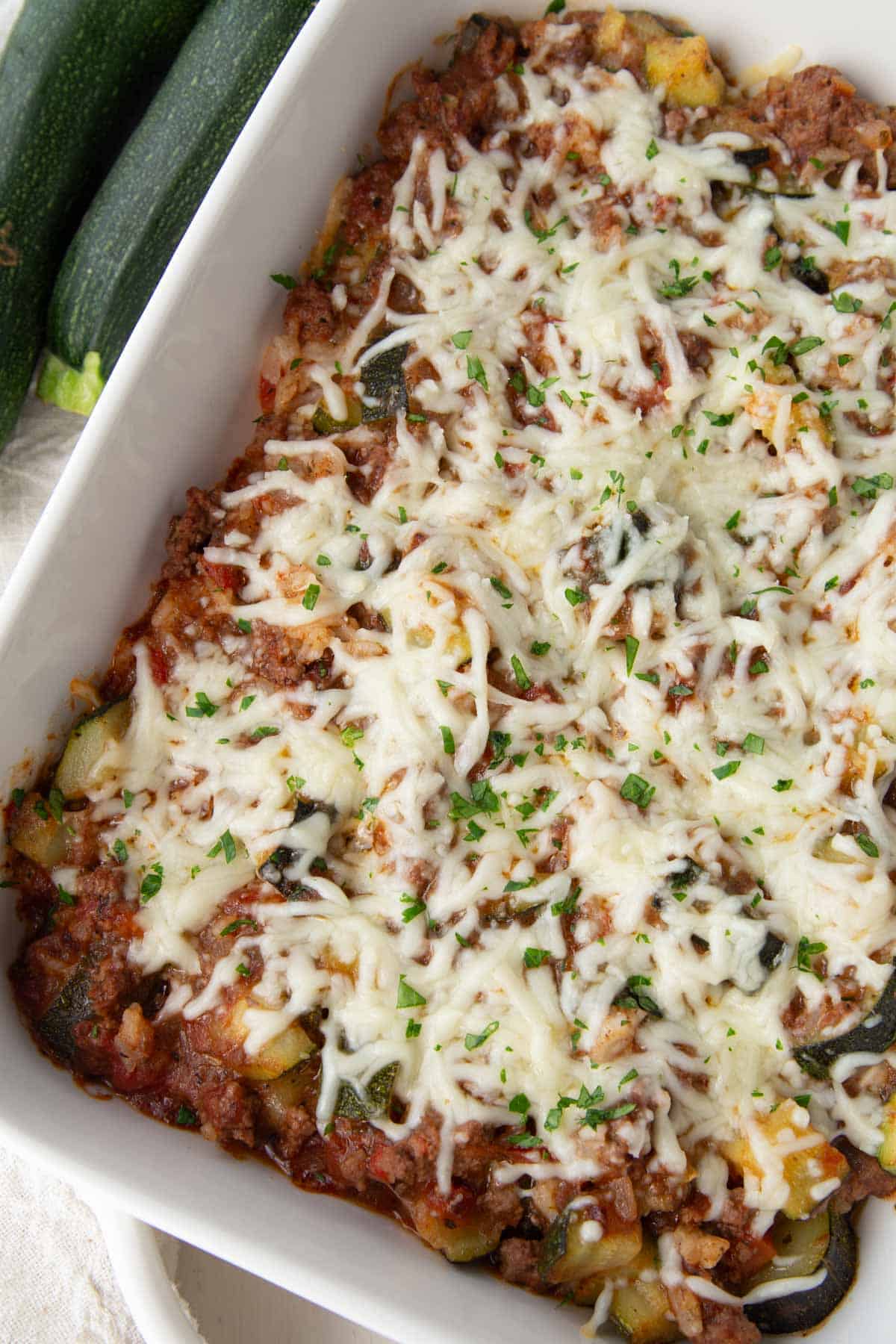 zucchini, ground beef, and tomatoes in a casserole dish topped with shredded cheese.