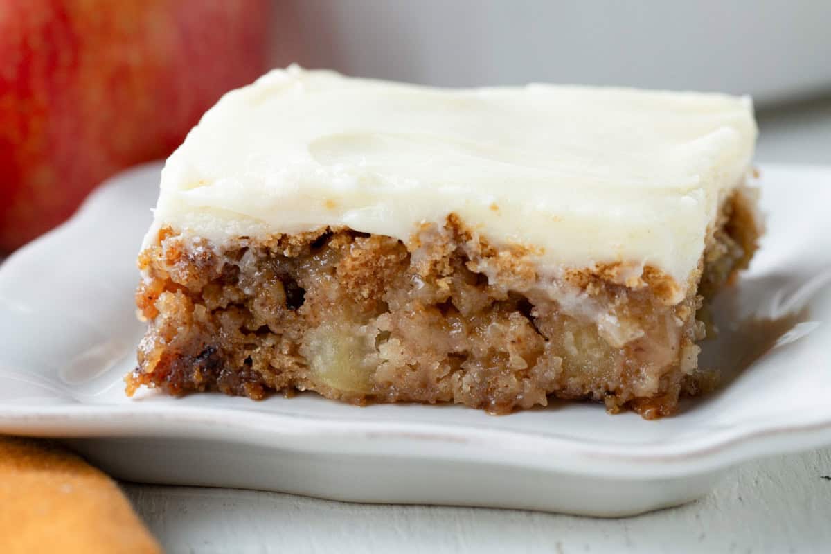 slice of apple cake with cream cheese frosting on a white plate.