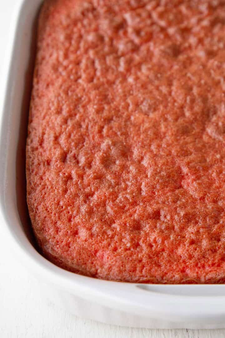 baked pink/red hued cake in a white cake pan.