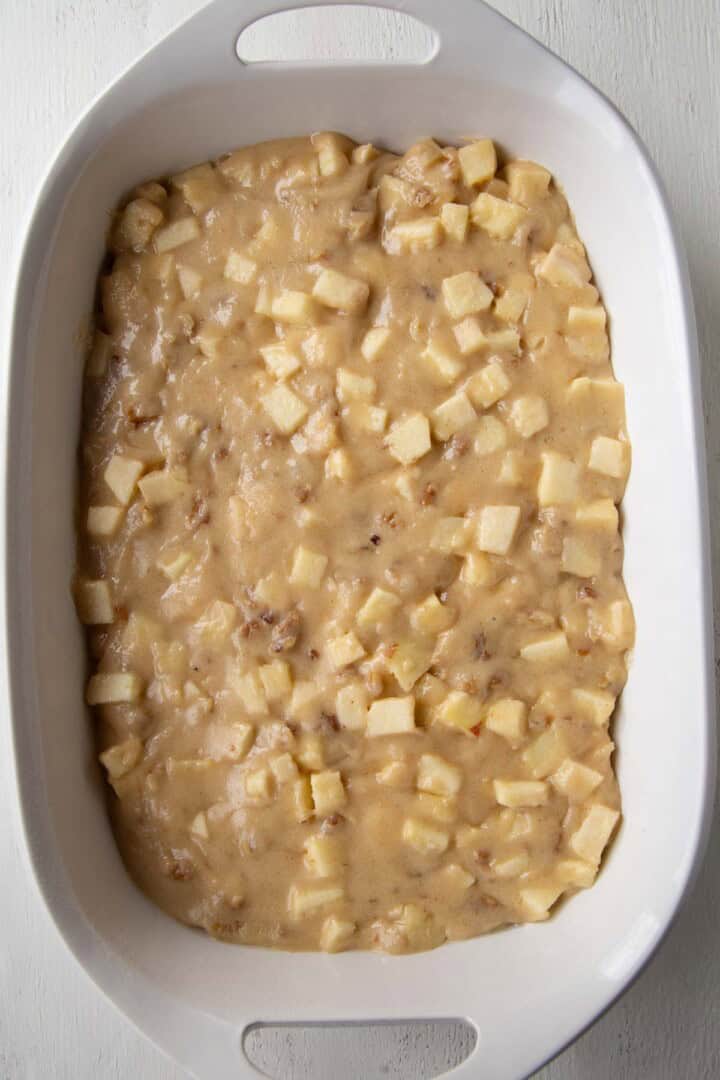 brown cake batter with pieces of apples in a 13x9 inch baking dish.