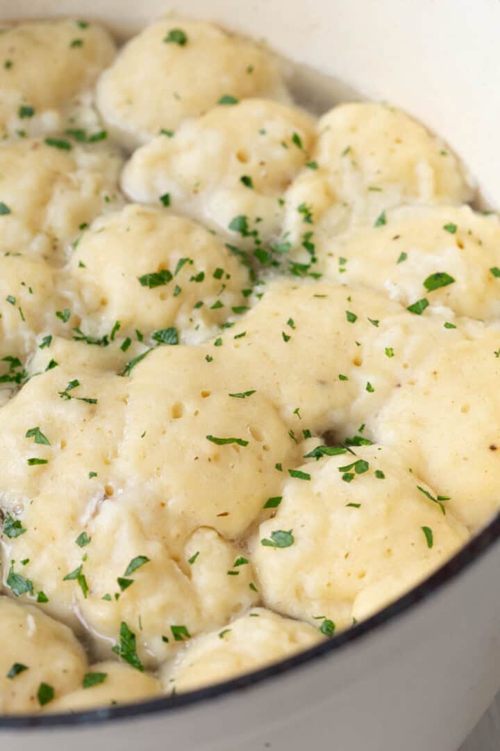 fluffy dumplings in a large pot, topped with chopped parsley.