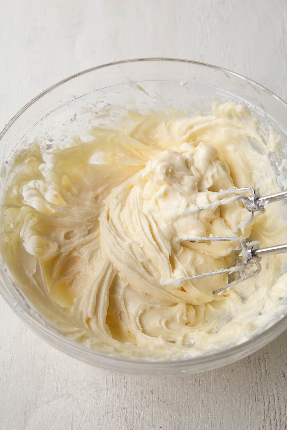 cream cheese frosting with a hand mixer in a glass bowl.