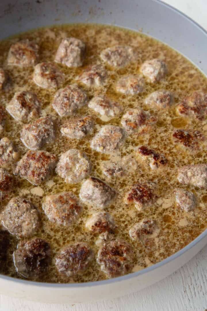 small meatballs cooking in broth in a skillet.