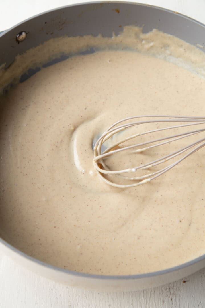 glossy sour cream sauce in a skillet with a whisk.