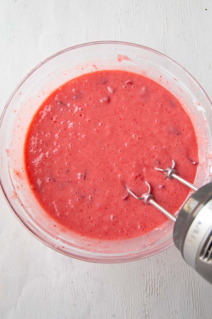 bright pink strawberry cake batter in a bowl with a hand mixer.