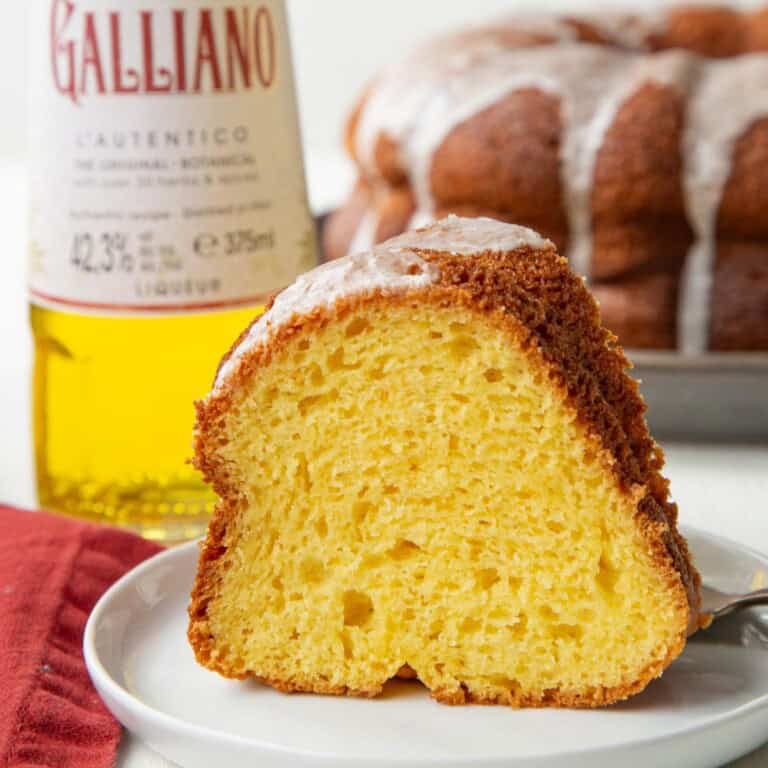 slice of yellor/orange bundt cake with a bottle of galliano behind it.
