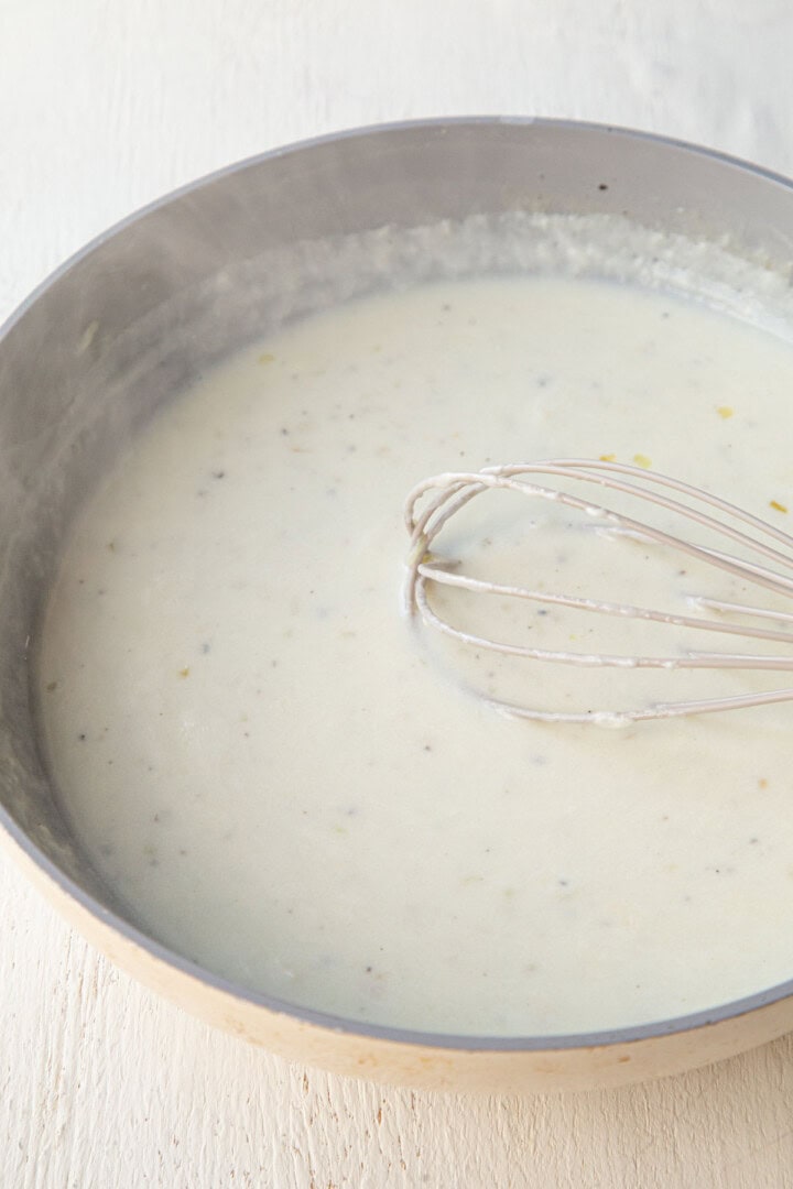a white creamy sauce in a skillet with a whisk.