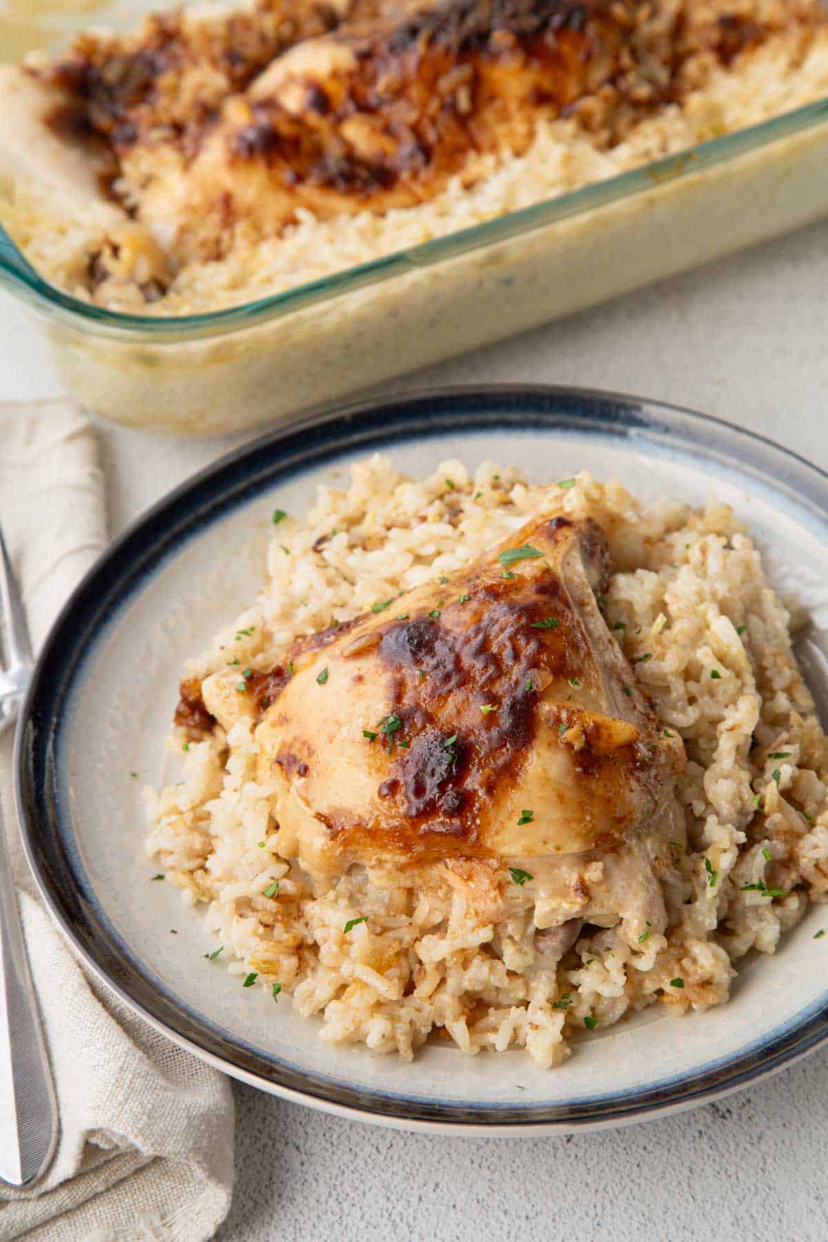chicken thigh on top of creamy rice on a plate with a casserole of more chicken and rice next to it.