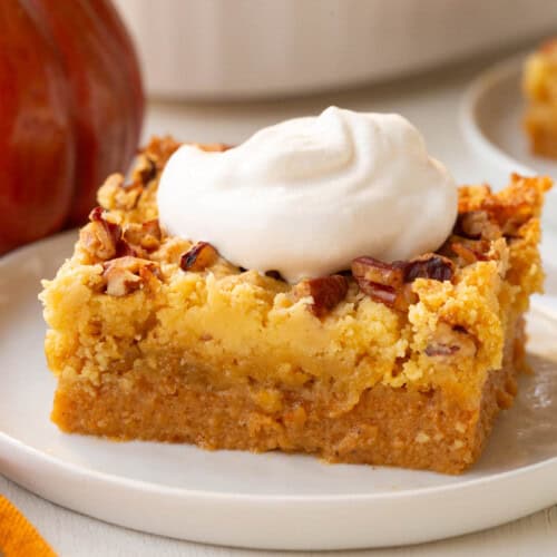 slice of cake with a pumpkin layer on the bottom, a cake layer in the middle, and pecans and whipped cream on top.
