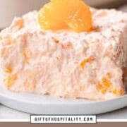 slice of fluffy, creamy gelatin salad with mandarin oranges inside and on top.