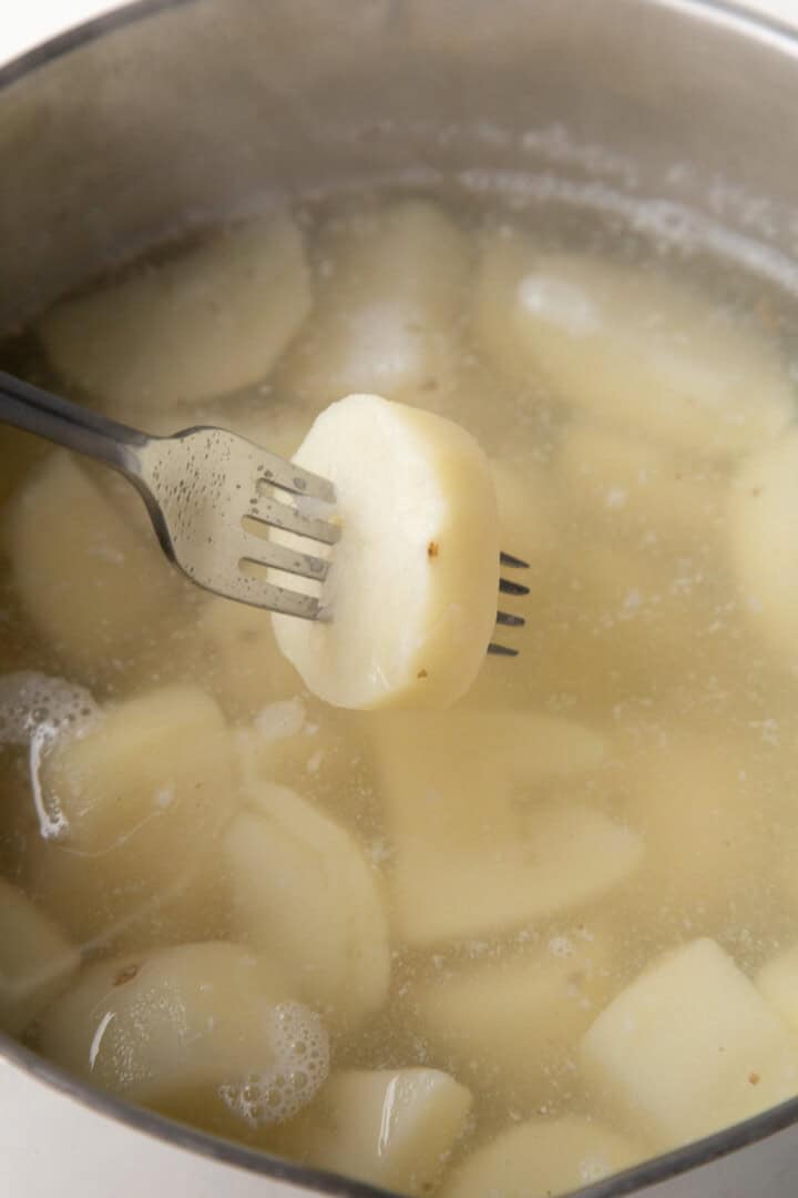 fork piercing a cooked potato above a pot of water and more potatoes.