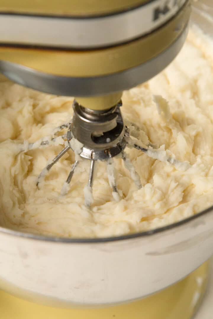 mashed potatoes in the bowl of a stand mixer with the whisk attachment.