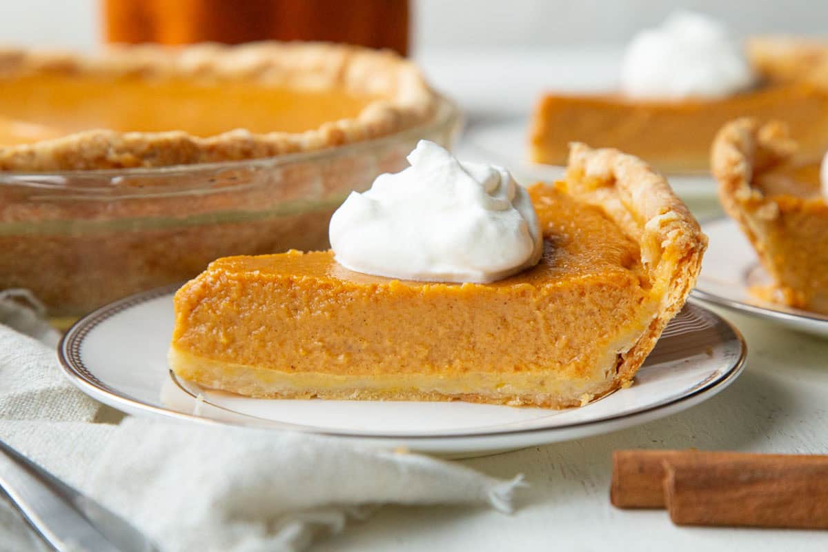 slice of pumpkin pie with a flaky crust and whipped cream on top.