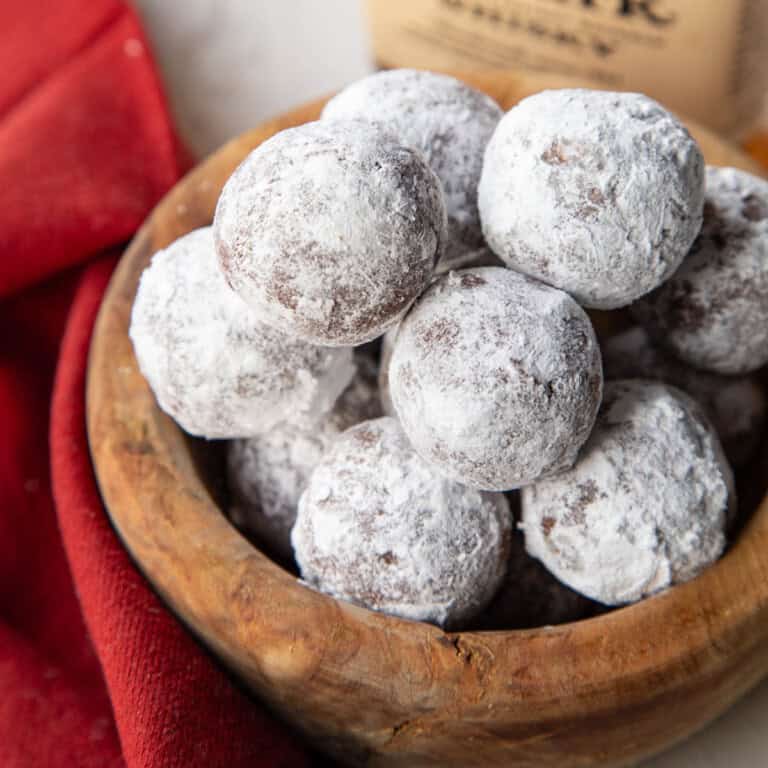 stack of bourbon balls coated in powdered sugar in a wooden bowl.