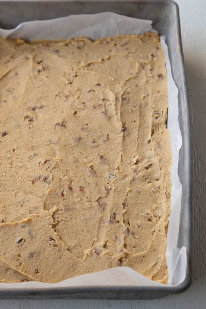 beige colored cookie dough with pecans in a metal pan.