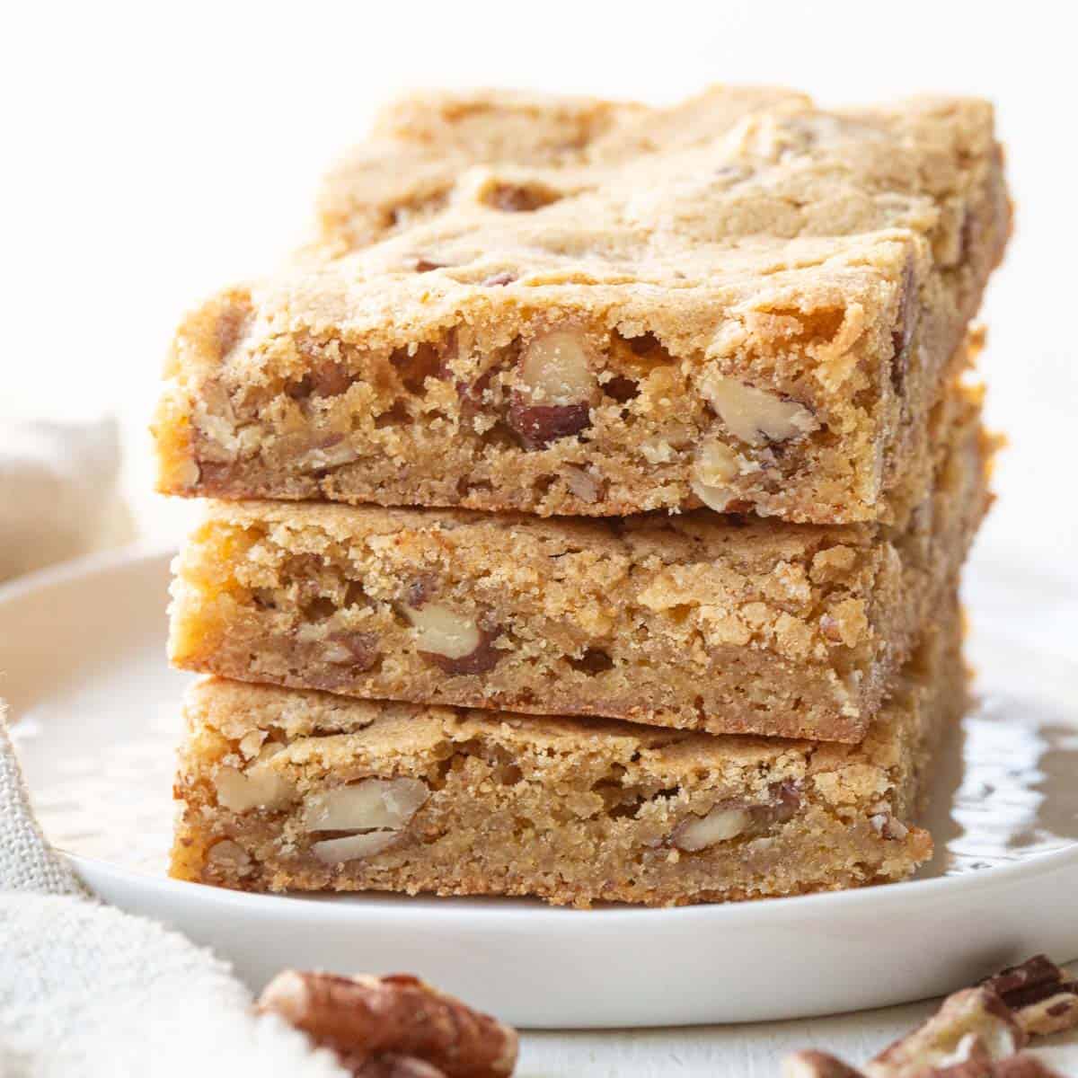 stack of three blondies with pecans inside on a white plate.