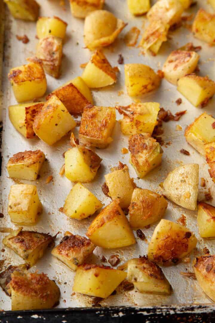 partially cooked cubed potatoes on a baking sheet with some crispy brown parts.