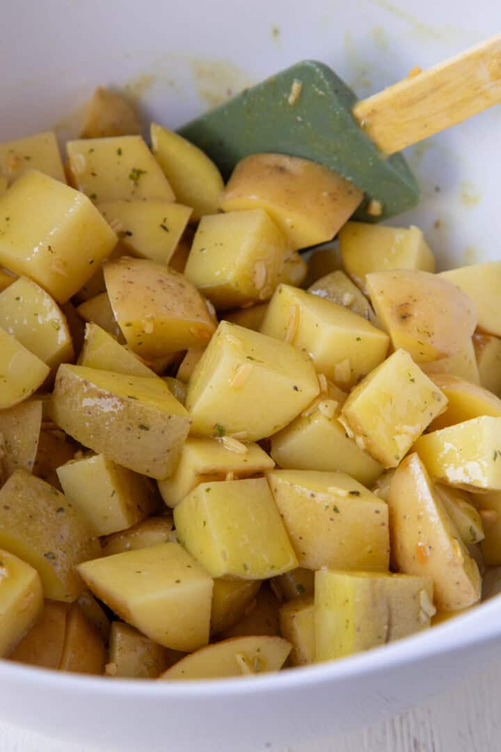 raw cubed potatoes coated in oil and onion soup mix in a bowl.
