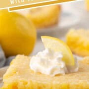 slice of lemon gooey butter cake with a yellow crust, yellow gooey layer, and whipped cream on top.