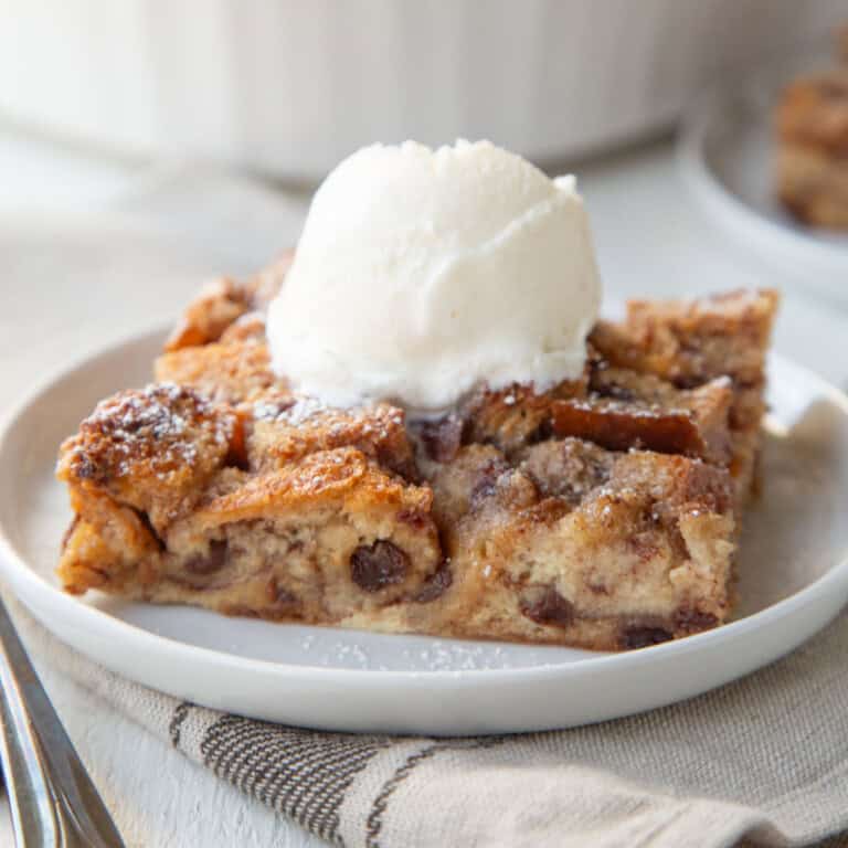 slice of raisin bread pudding on a white plate, topped with a scoop of vanilla ice cream.