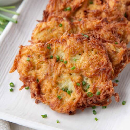crispy potato pancakes topped with chopped chives on a white platter.