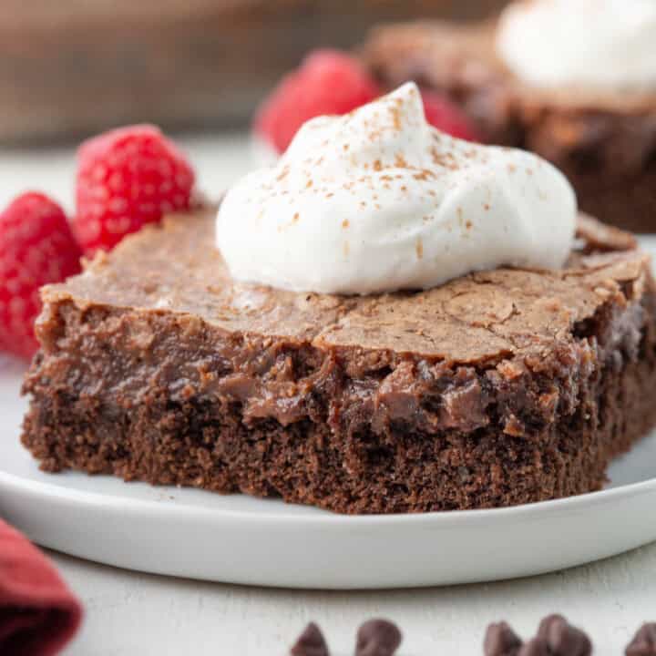 slice of chocolate gooey butter cake with two layers of chocolate, with a dollop of whipped cream on top.